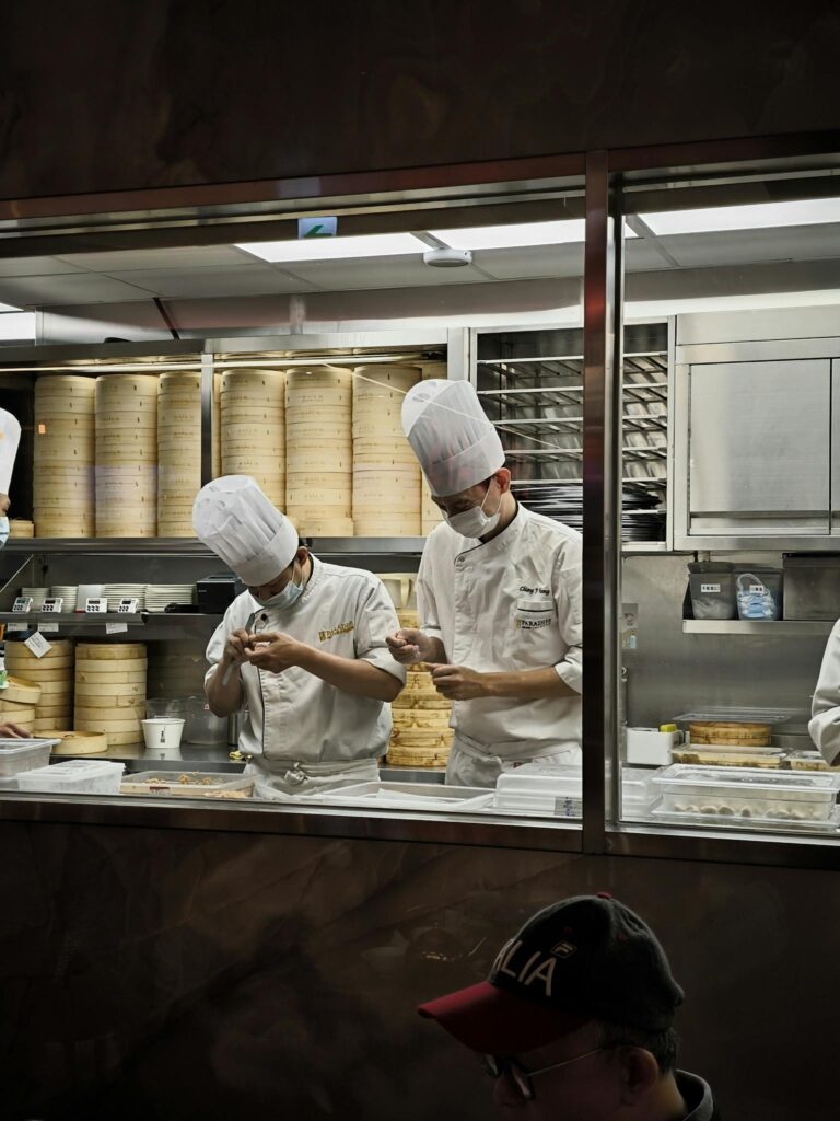 Two chefs expertly prepare dim sum in a restaurant kitchen, showcasing culinary skill.